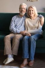 134421422-vertical-image-healthy-attractive-grey-haired-wife-and-husband-hugging-resting-on-couch-looking-at